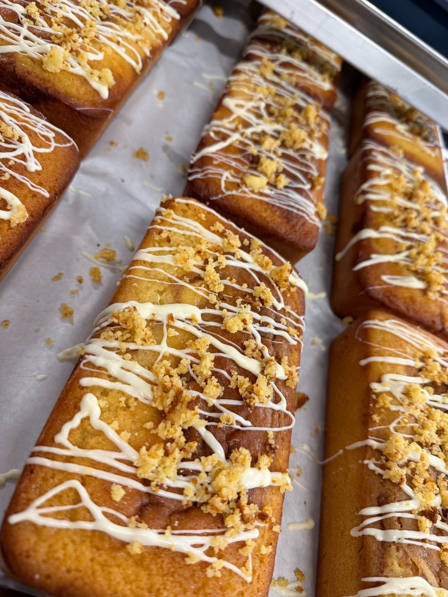 Close-up of several rectangular loaf cakes on a baking sheet, topped with white lilys chocolate icing and crumbly streusel-like crumbs.